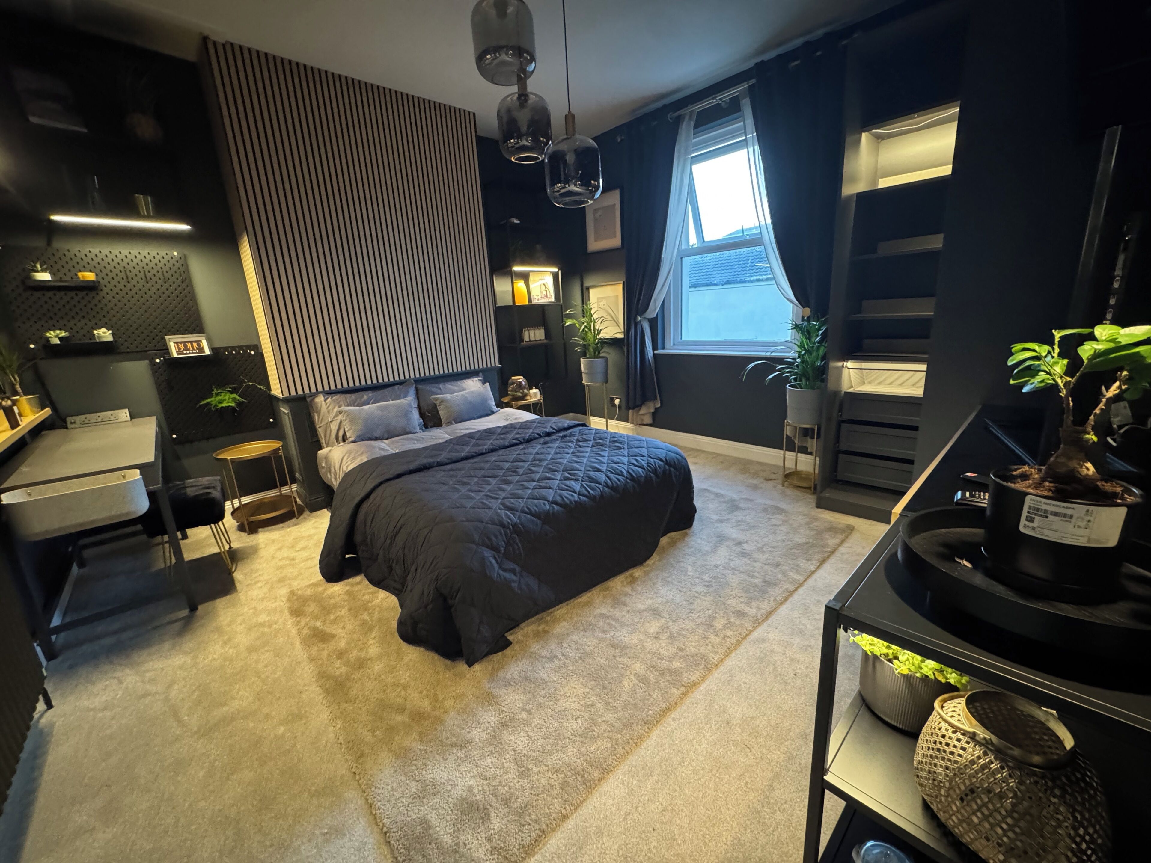 Een moderne slaapkamer met een groot bed, nachtkastjes, een bureau en een potplant.