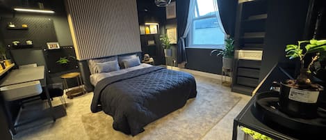 Een moderne slaapkamer met een groot bed, nachtkastjes, een bureau en een potplant.