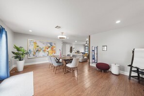 A modern living room with a dining area, a large abstract painting, and a staircase leading to an upper level. - Fabulous 3-bedroom deep lounging Pool house with AC & Arcade in vibrant Houston (Houston)