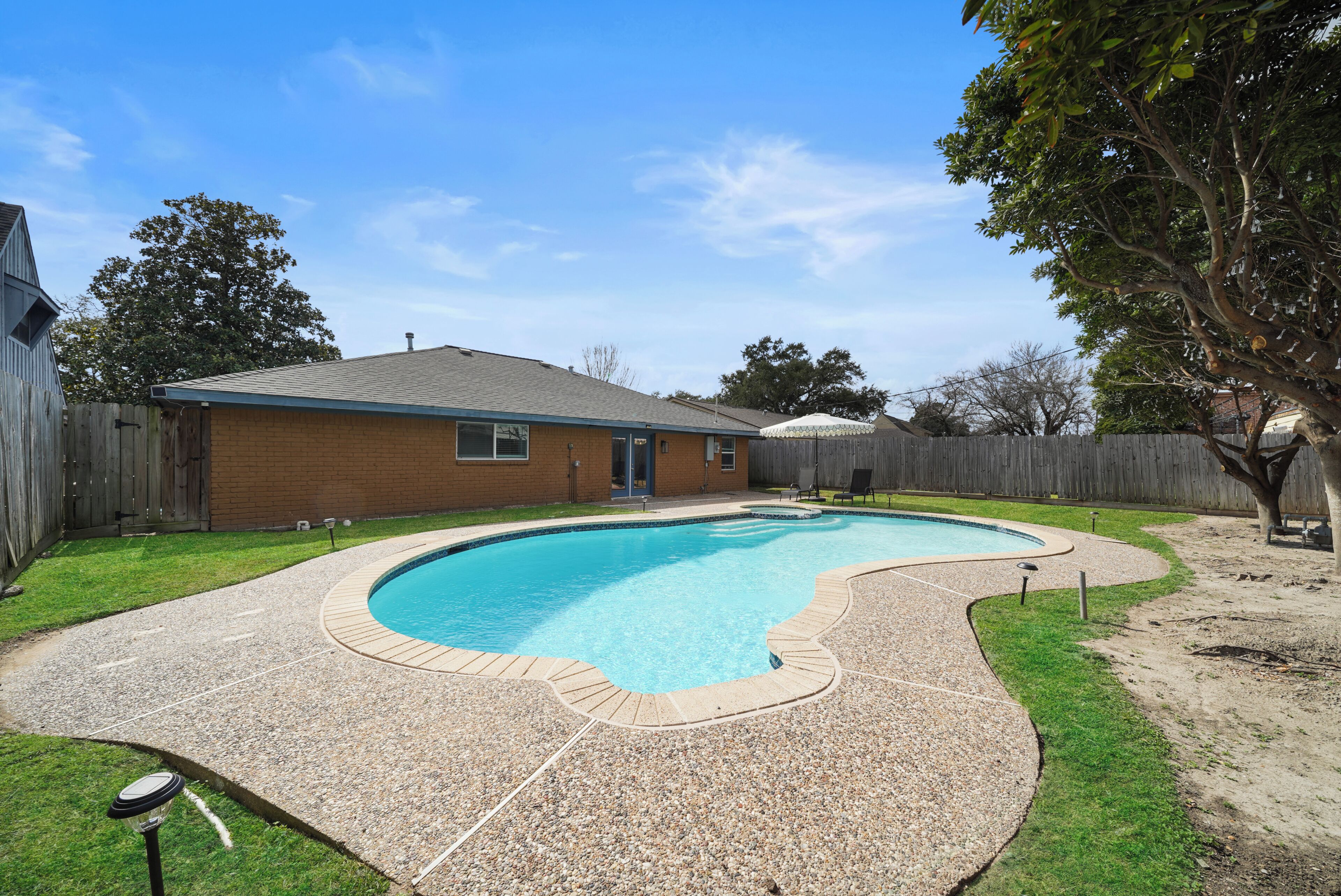 A backyard with a swimming pool, a wooden fence, and a house.