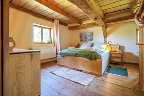 Ein Schlafzimmer mit Holzboden, einem Bett mit grüner Decke, einem Nachttisch mit Lampe und einem Fenster mit Vorhängen.
