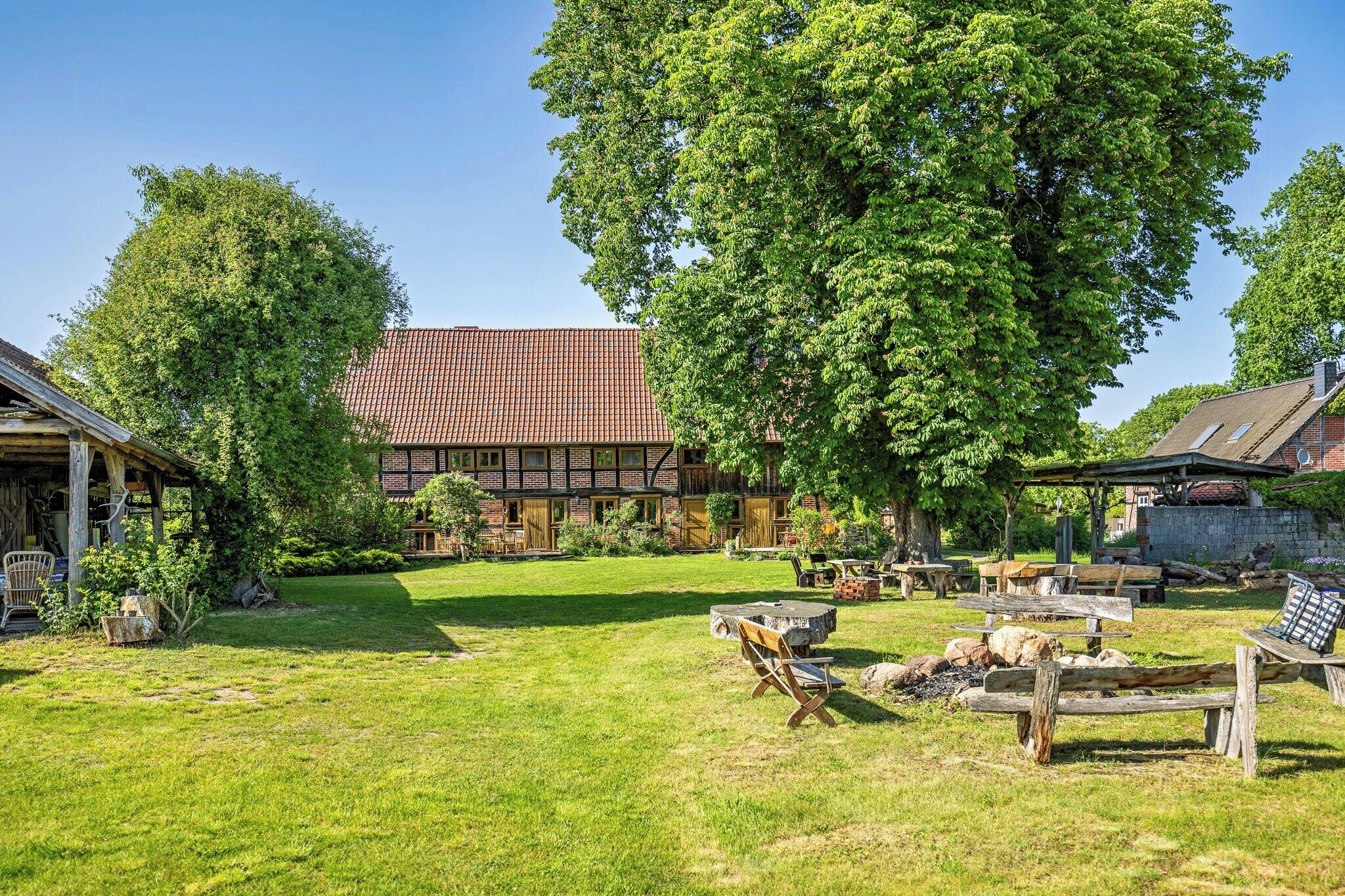 A traditional half-timbered house with a large tree in the yard, outdoor seating, and a fire pit.
