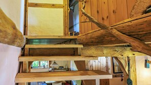 Interior de madera con una escalera que sube a un nivel superior, un ventanal visible y una puerta con picaporte de madera.