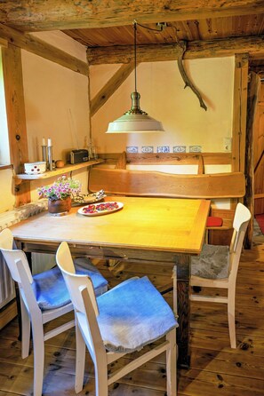 Ein rustikaler Essbereich aus Holz mit einem großen Tisch, zwei Stühlen und einer hängenden Leuchte.