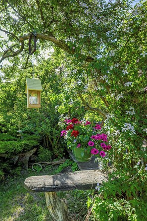 A garden with a wooden bench, a hanging bird feeder, and a potted plant with flowers. - Eco-friendly farmhouse with a garden by the river (Zehrental)