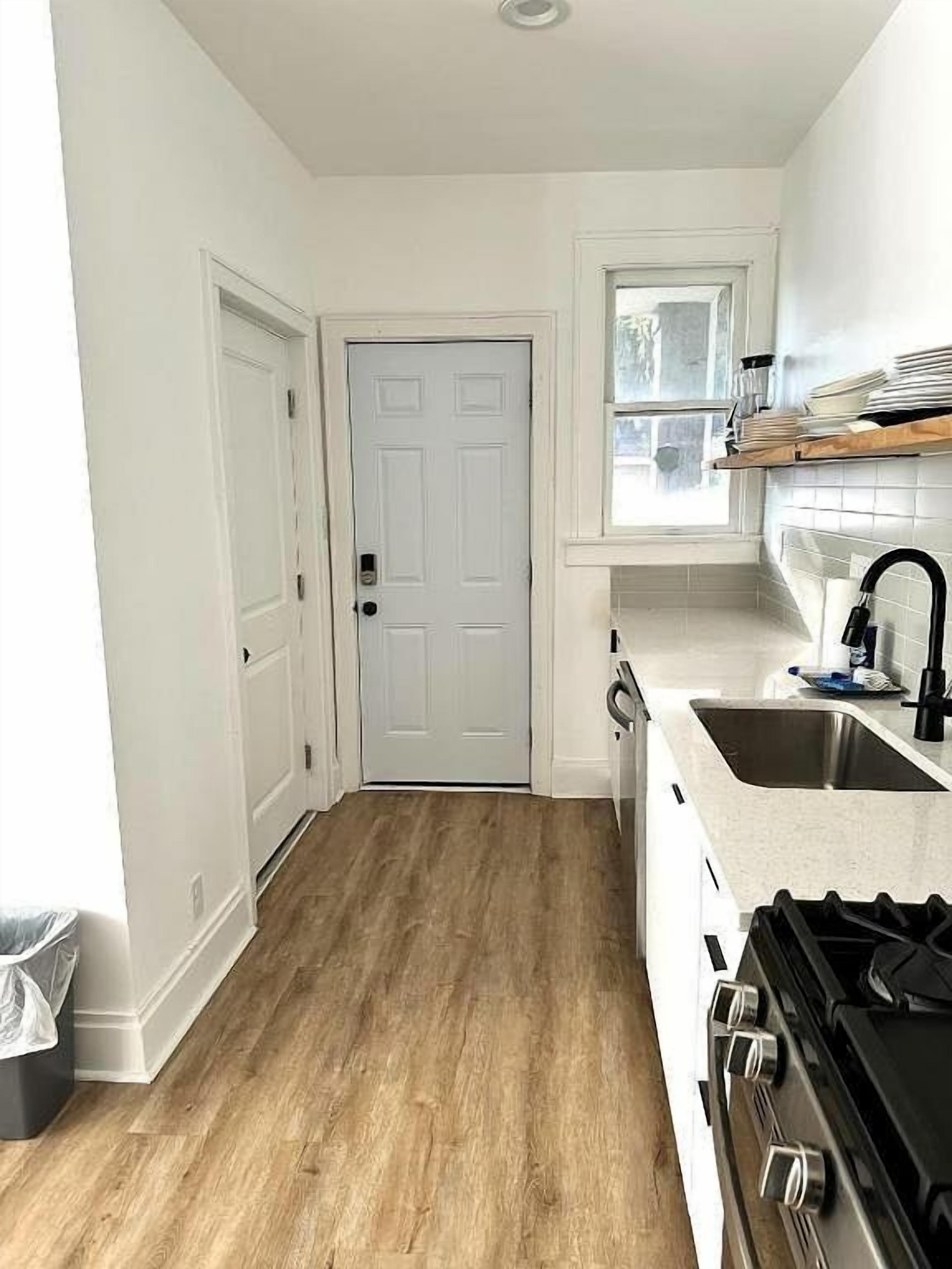 A kitchen with a white door, a window, a sink, and a stove.