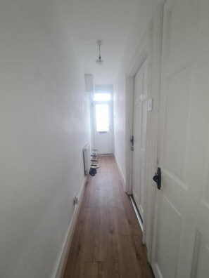 A narrow hallway with wooden flooring, white walls, and a door on the right.