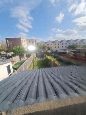 A residential area with a sloped roof, a fenced yard, and a row of buildings in the background. - The Oaks (Grays)