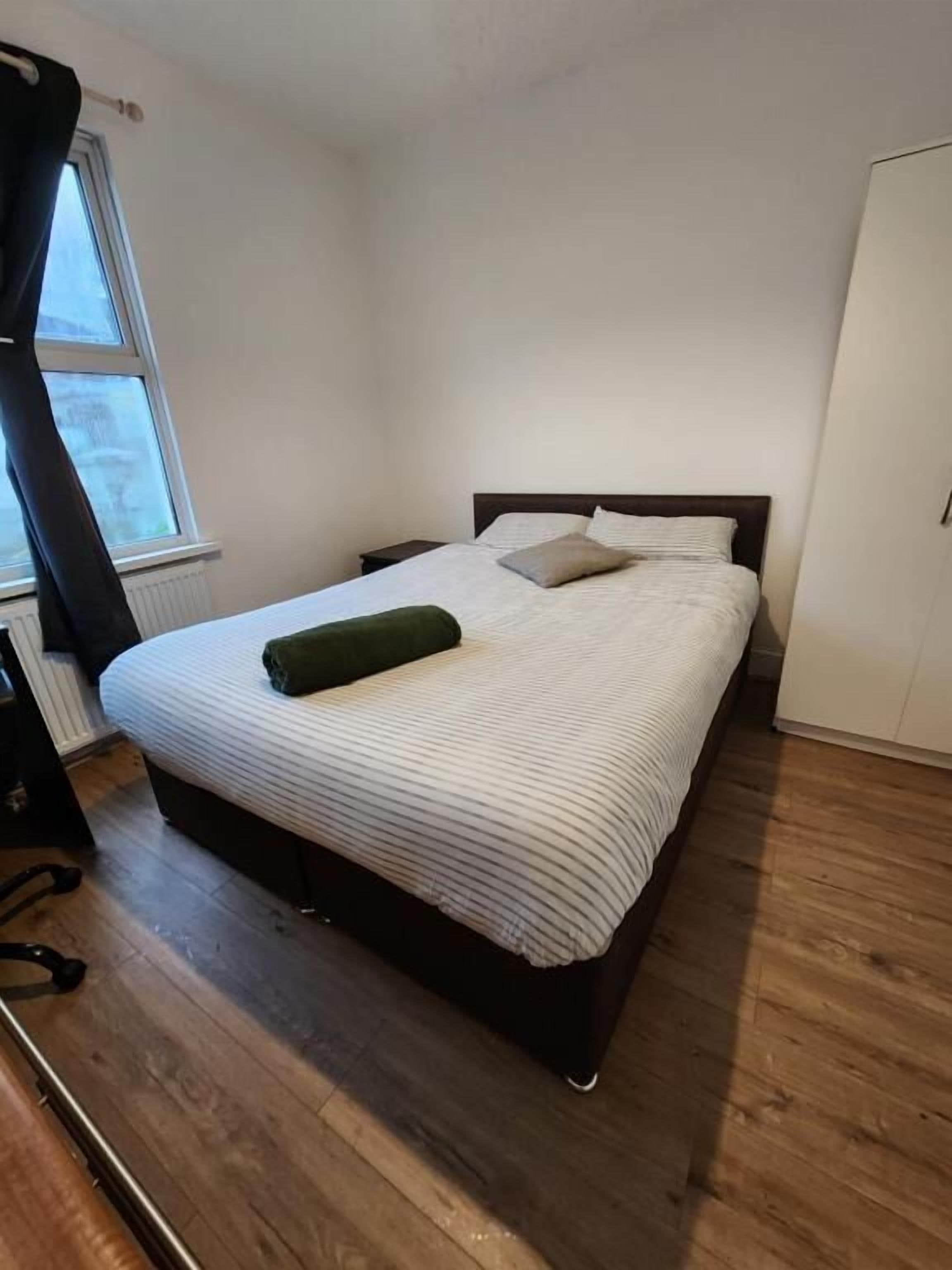 Una cama individual con colcha a rayas blancas y grises, un almohadón verde y suelo de madera.