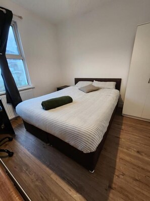 A single bed with a white and gray striped bedspread, a green pillow, and a wooden floor. - The Oaks (Grays)