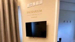 Habitación de hotel con televisor de pantalla plana montado en la pared, cortina y puerta que da a un baño con toallero.