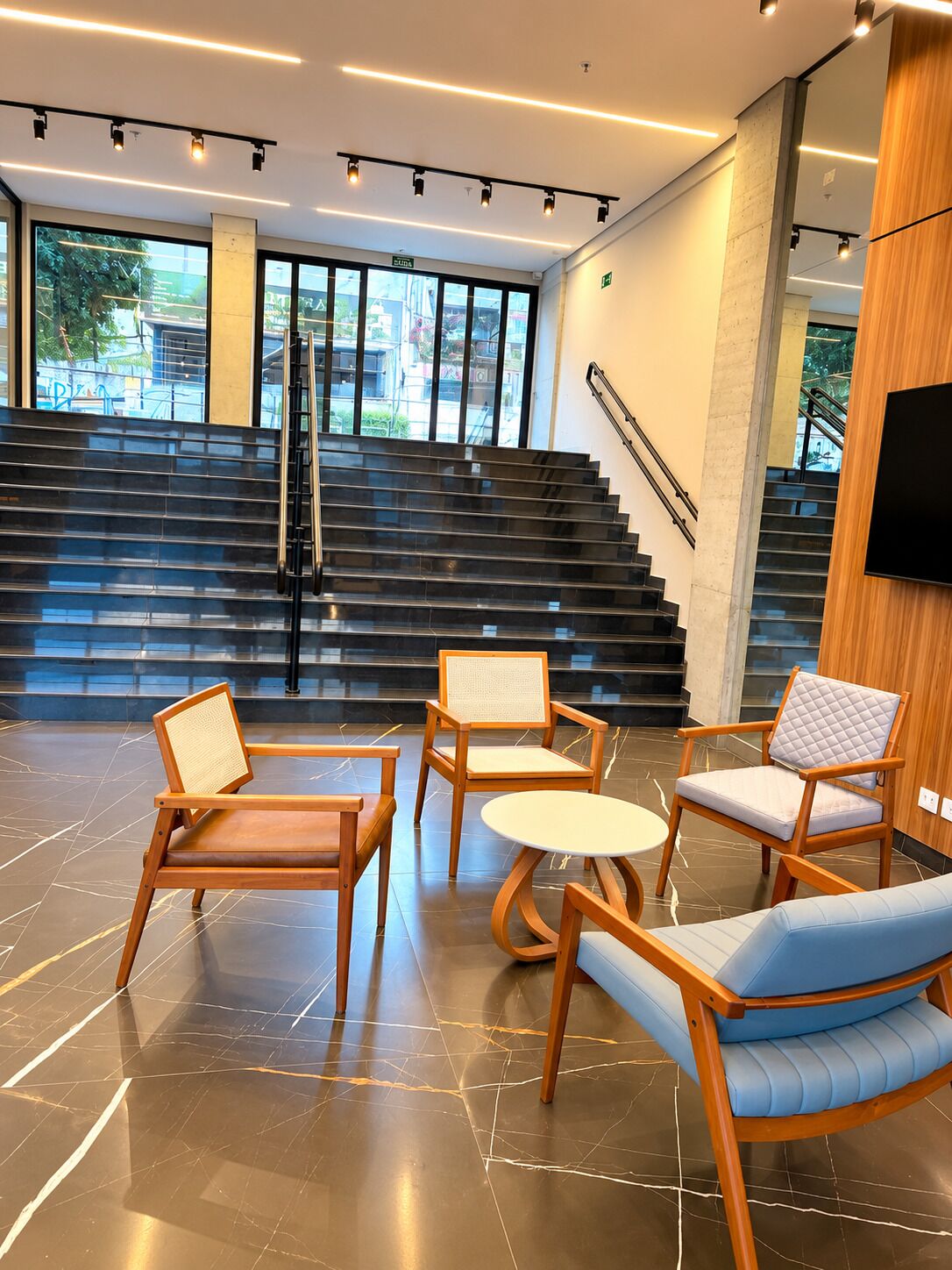 A modern lobby with a staircase, seating area, and a TV mounted on the wall.