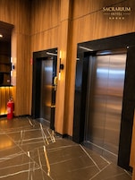 A modern elevator area with wood paneling and marble flooring, featuring a fire extinguisher and a visible emergency exit sign.