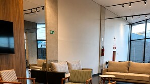 Vestíbulo de hotel con diseño moderno, que incluye un sofá grande, varios sillones, una mesita redonda y un televisor de pantalla plana montado en la pared.