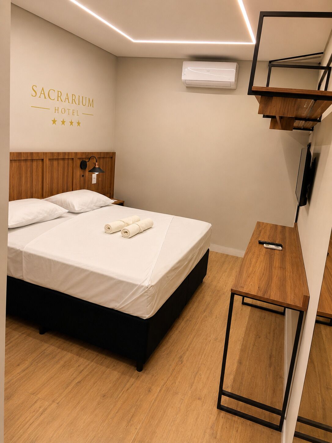 Habitación de hotel con cama, mesita de noche, aire acondicionado instalado en la pared y un letrero que dice 'SACRARIUM HOTEL'.