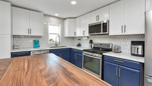 A modern kitchen with white cabinets, a wooden countertop, stainless steel appliances, and a tiled backsplash. - Holds 8 · Pool · 3BR/2BA Upper Duplex Peacock Horse Beach Nearby Out City Life (Galveston)