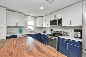 Eine moderne Küche mit weißen Schränken, einer Holz Arbeitsplatte, Edelstahlgeräten und einer gefliesten Spritzschutzwand.