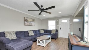 A living room with a sectional sofa, a coffee table, a ceiling fan, and a door. - Holds 8 · Pool · 3BR/2BA Upper Duplex Peacock Horse Beach Nearby Out City Life (Galveston)
