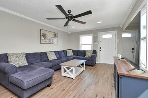 Ein Wohnzimmer mit Ecksofa, Couchtisch, Deckenventilator und einer Tür.