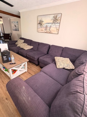 Ein Wohnzimmer mit einem Ecksofa, einem Couchtisch und einem Gemälde von einer Strandansicht.