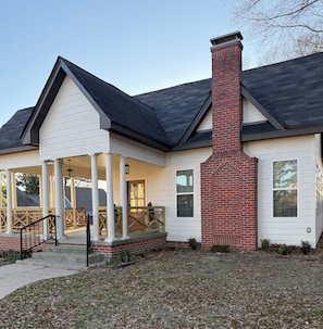 A two-story house with a covered porch, a brick chimney, and a front entrance with steps.