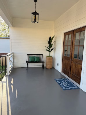 A porch with a bench, a potted plant, a door, and a welcome mat.