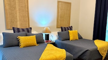A hotel room with two beds, a bedside table, a lamp, and a window with curtains.