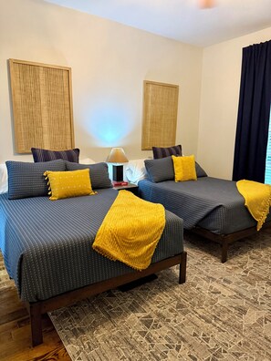 Habitación de hotel con dos camas, una mesita de noche, una lámpara y una ventana con cortinas.