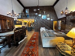 A spacious living area with a staircase, wooden flooring, a sofa, a dining table, and a chandelier. - Whispering Waters Retreat (South Fork)