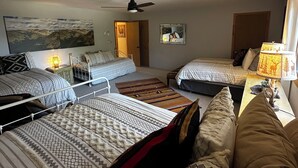 Ein Zimmer mit drei Betten, einem Deckenventilator, einem Gemälde, einem Spiegel und einer Lampe.