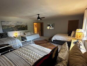 Ein Zimmer mit drei Betten, einem Deckenventilator, einem Gemälde, einem Spiegel und einer Lampe.