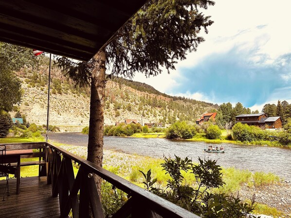 A riverside view from a wooden deck with a river, houses, and a boat. - Whispering Waters Retreat (South Fork)