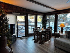 A cozy room with a wooden interior, a dining table with chairs, a sofa, and a large window overlooking a snowy landscape.