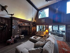 A cozy living room with a stone fireplace, a large sofa, and a deer head mounted on the wall.