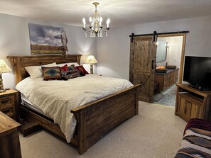 Een slaapkamer met een houten bed, een kroonluchter, een schilderij, een dressoir en een televisie.