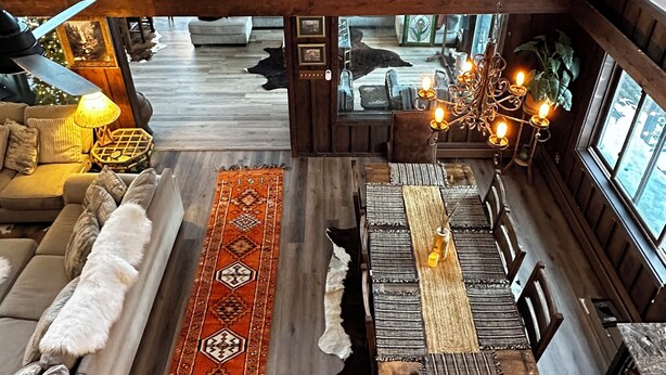 Ein Zimmer mit hohen Decken, Holzboden, einem Essbereich mit langem Tisch und einer Couch mit gemustertem Teppich.