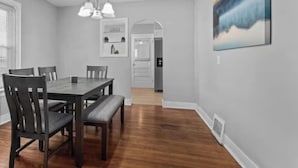 A dining area with a wooden table, chairs, and a bench. There is a chandelier above the table and a painting on the wall.