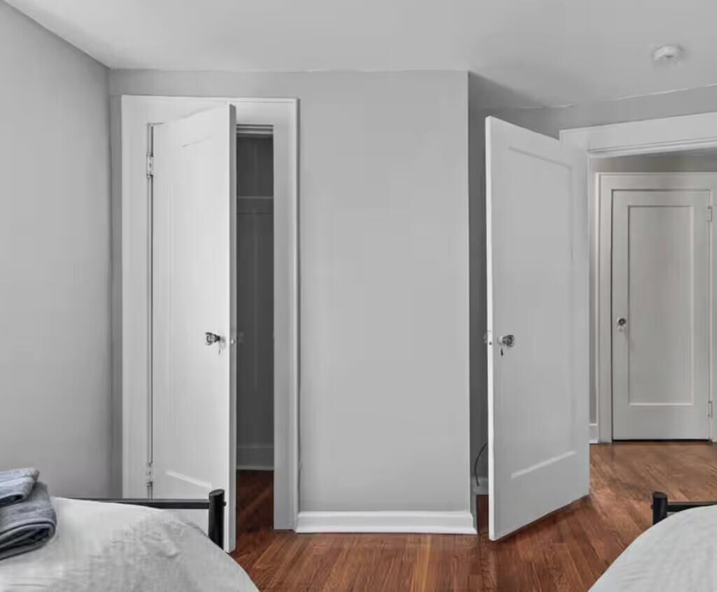 Quarto de hotel com duas camas, piso de madeira e porta branca.