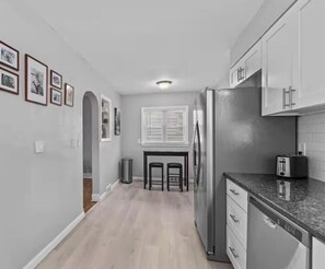 A kitchen with a refrigerator, a toaster, and a sink. There are two stools and a window with blinds.