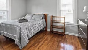 Un dormitorio con cama, una silla de madera, un aparador y una ventana con persianas.
