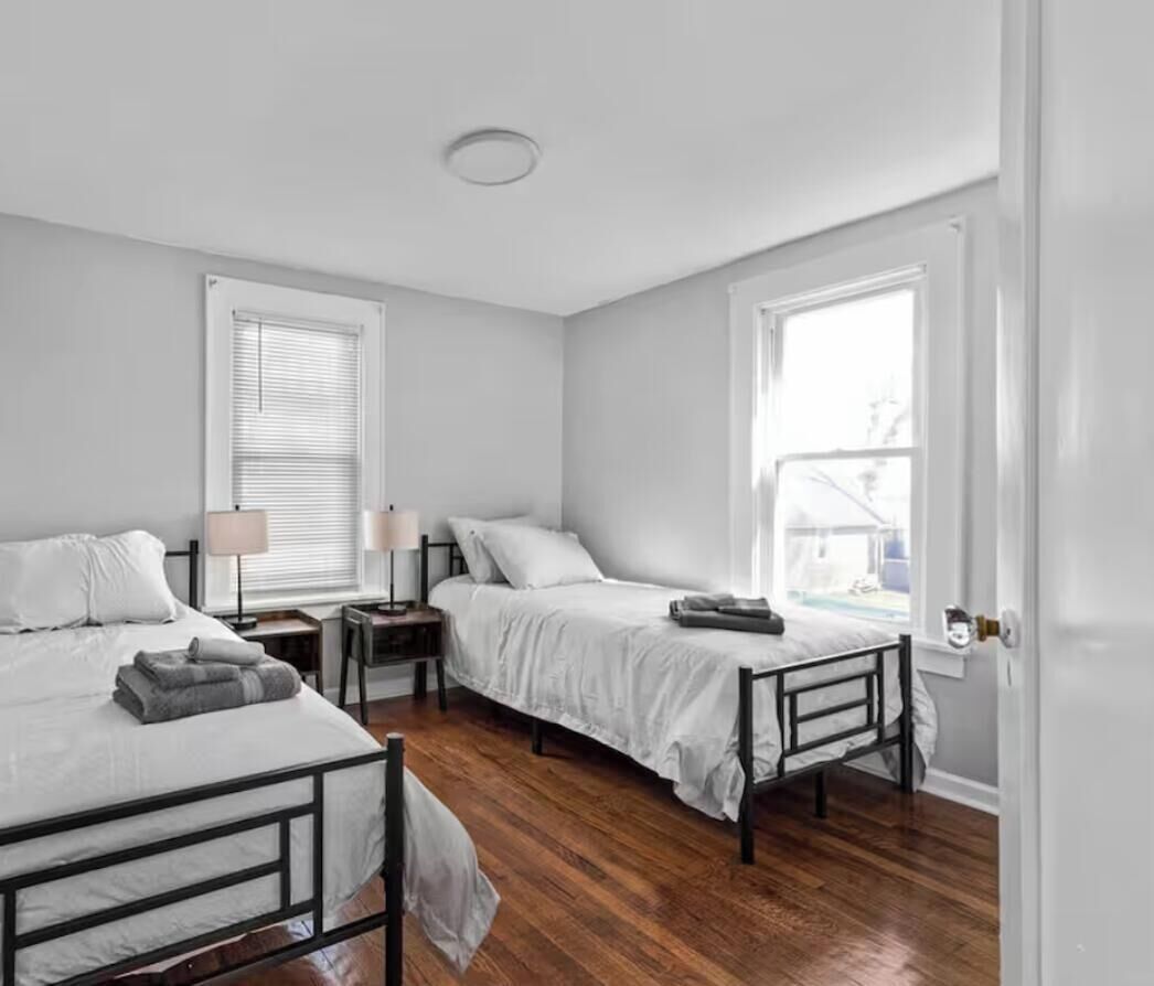 A bedroom with two single beds, wooden flooring, bedside tables with lamps, and a window with blinds.