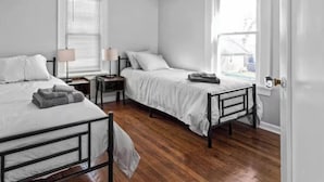 A bedroom with two single beds, wooden flooring, bedside tables with lamps, and a window with blinds.
