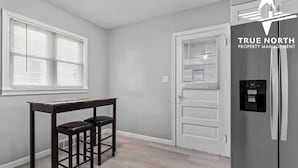 Una cocina con refrigerador, una mesa de comedor con sillas y una puerta con ventana.