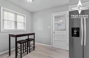 A kitchen with a refrigerator, a dining table with chairs, and a door with a window.