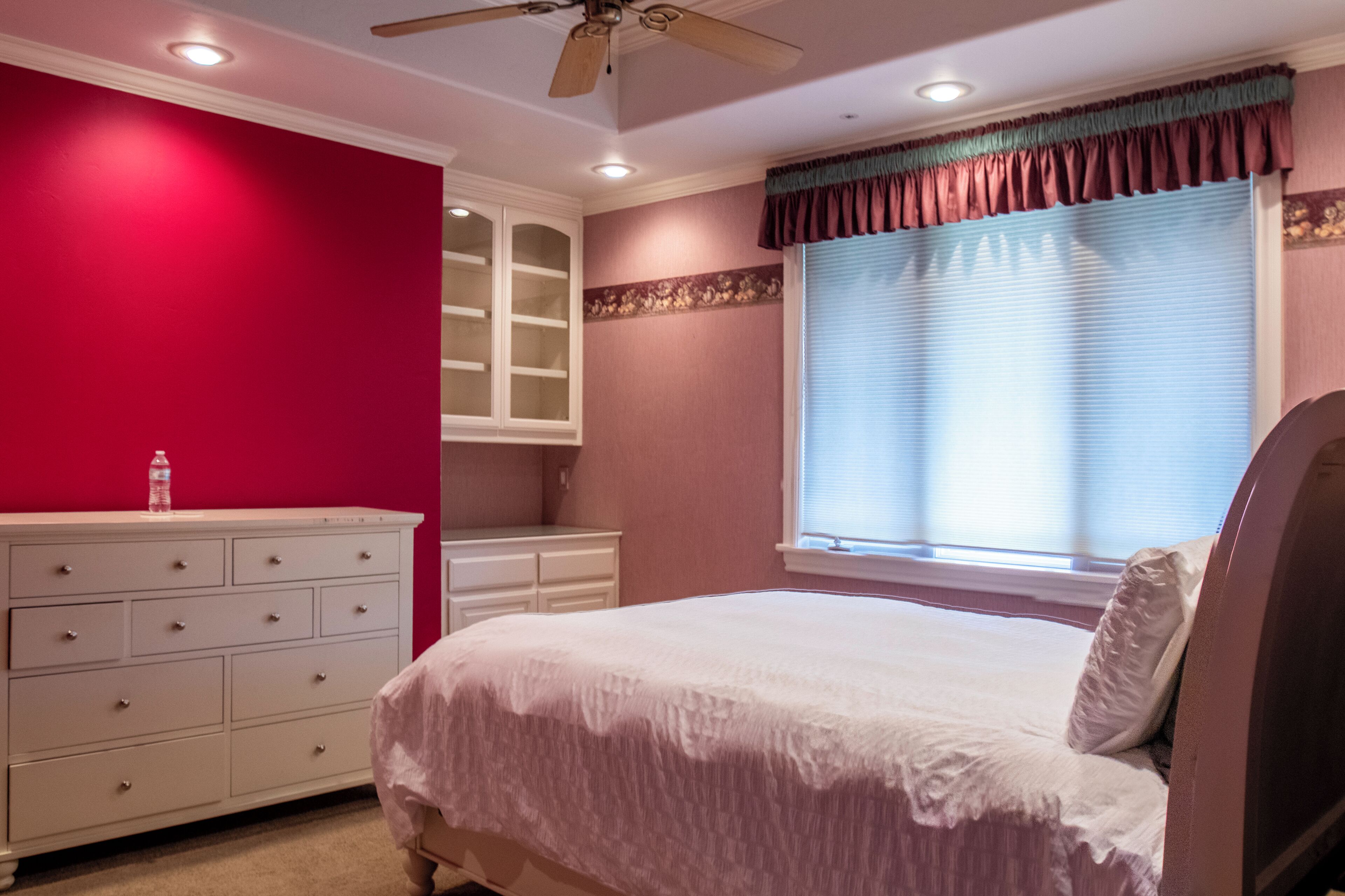 Un dormitorio con cama, cómoda, ventana con persianas y ventilador de techo.