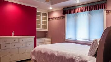 Un dormitorio con cama, cómoda, ventana con persianas y ventilador de techo.