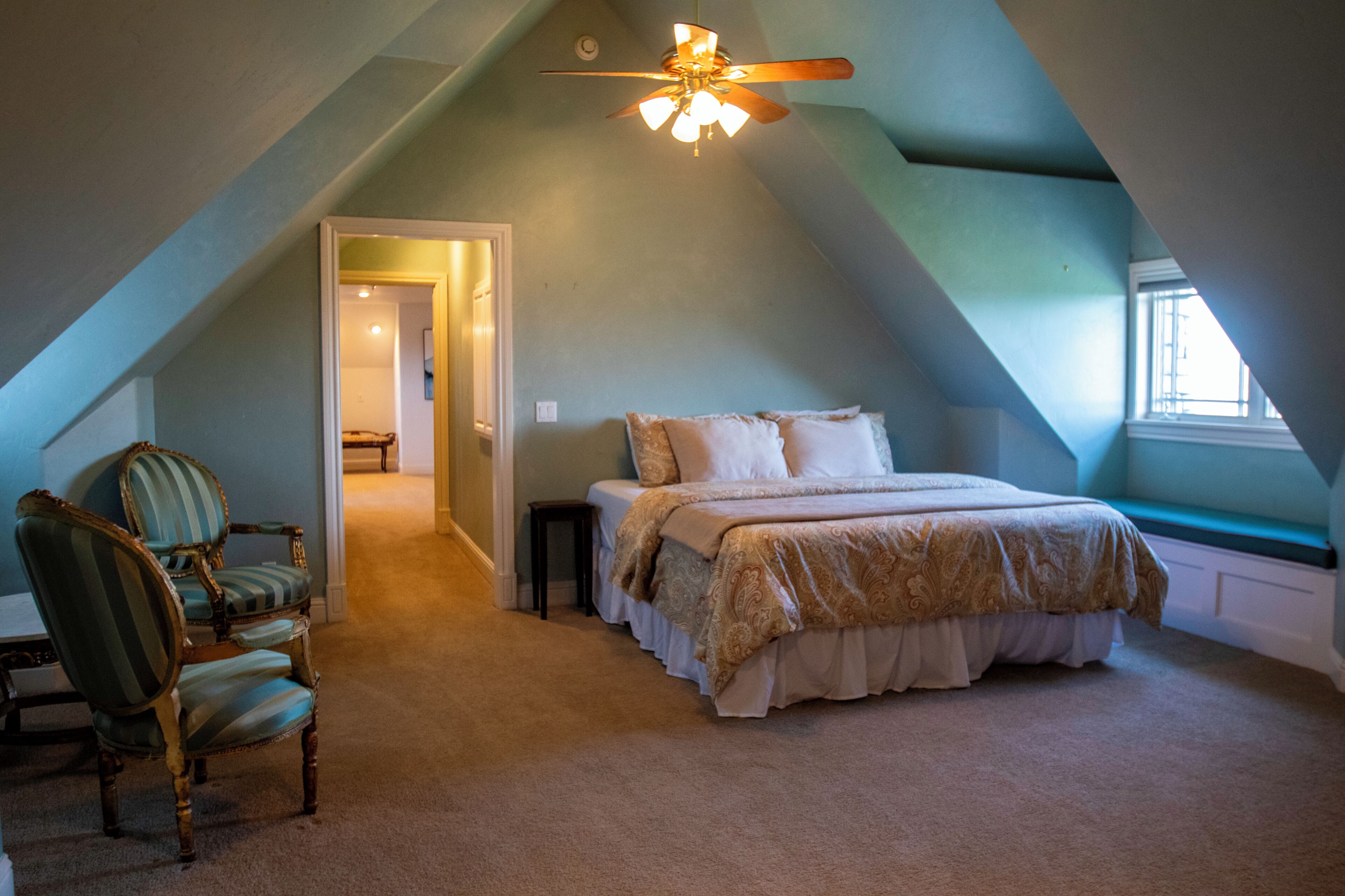A bedroom with a sloped ceiling, a bed with a patterned bedspread, a chair, and a window.