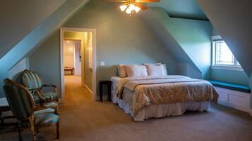 A bedroom with a sloped ceiling, a bed with a patterned bedspread, a chair, and a window.