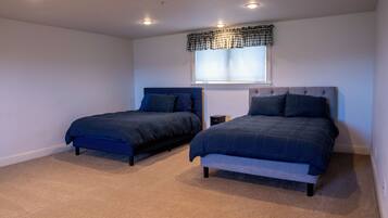 A bedroom with two beds, a window with blinds, and recessed ceiling lights.