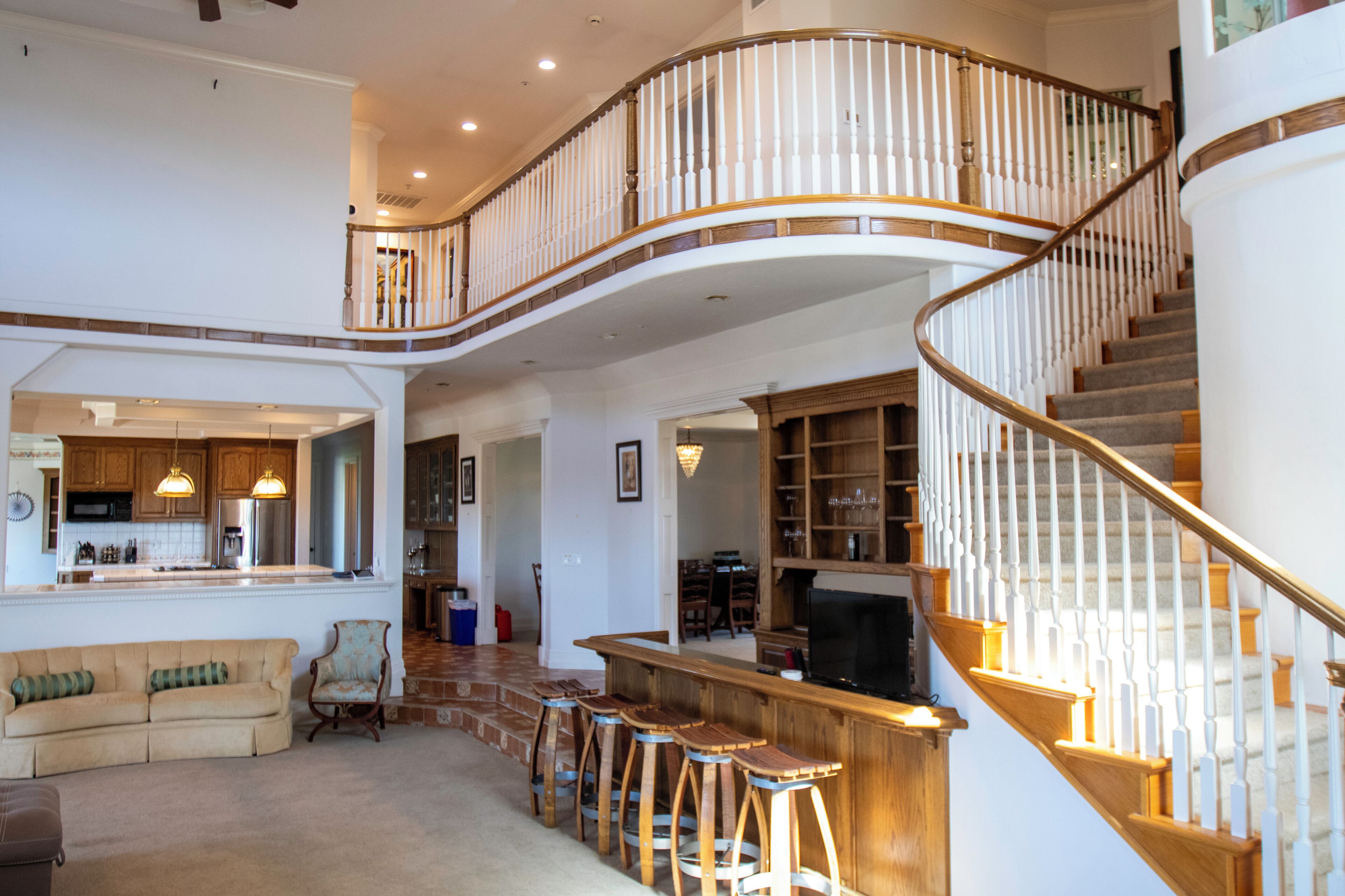A spacious living area with a curved staircase, a kitchen, and a bar area.